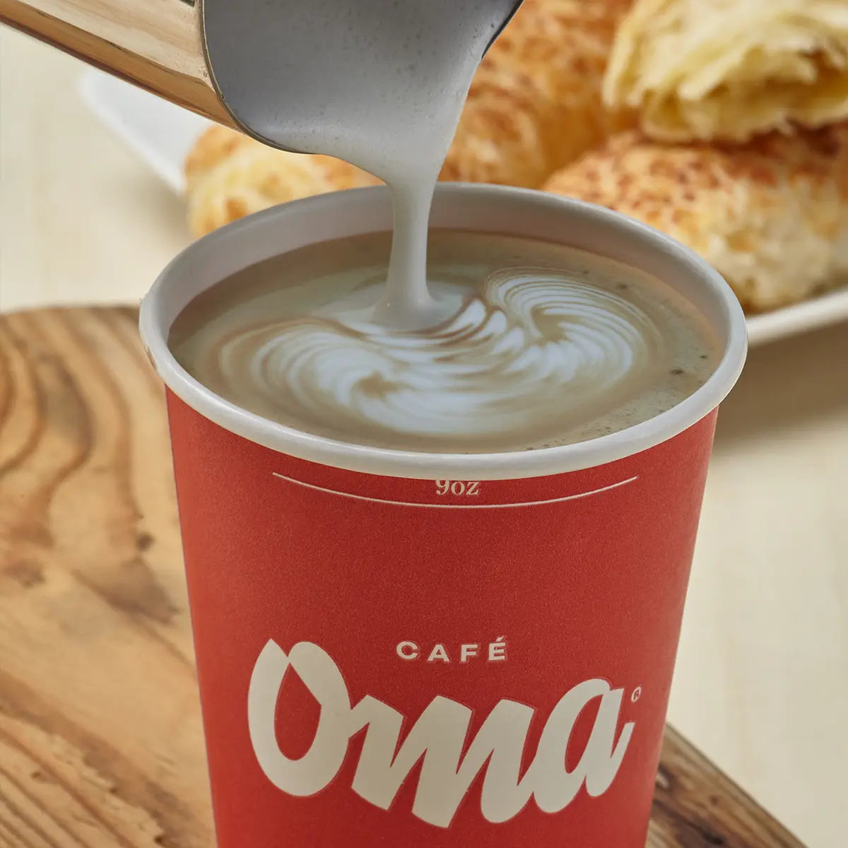 Variedad de bebidas calientes de Café Oma: tinto colombiano, americano, chocolate, infusiones, té chai y espresso servidos en tazas rojas con el logo de Oma sobre una mesa de madera cálida.